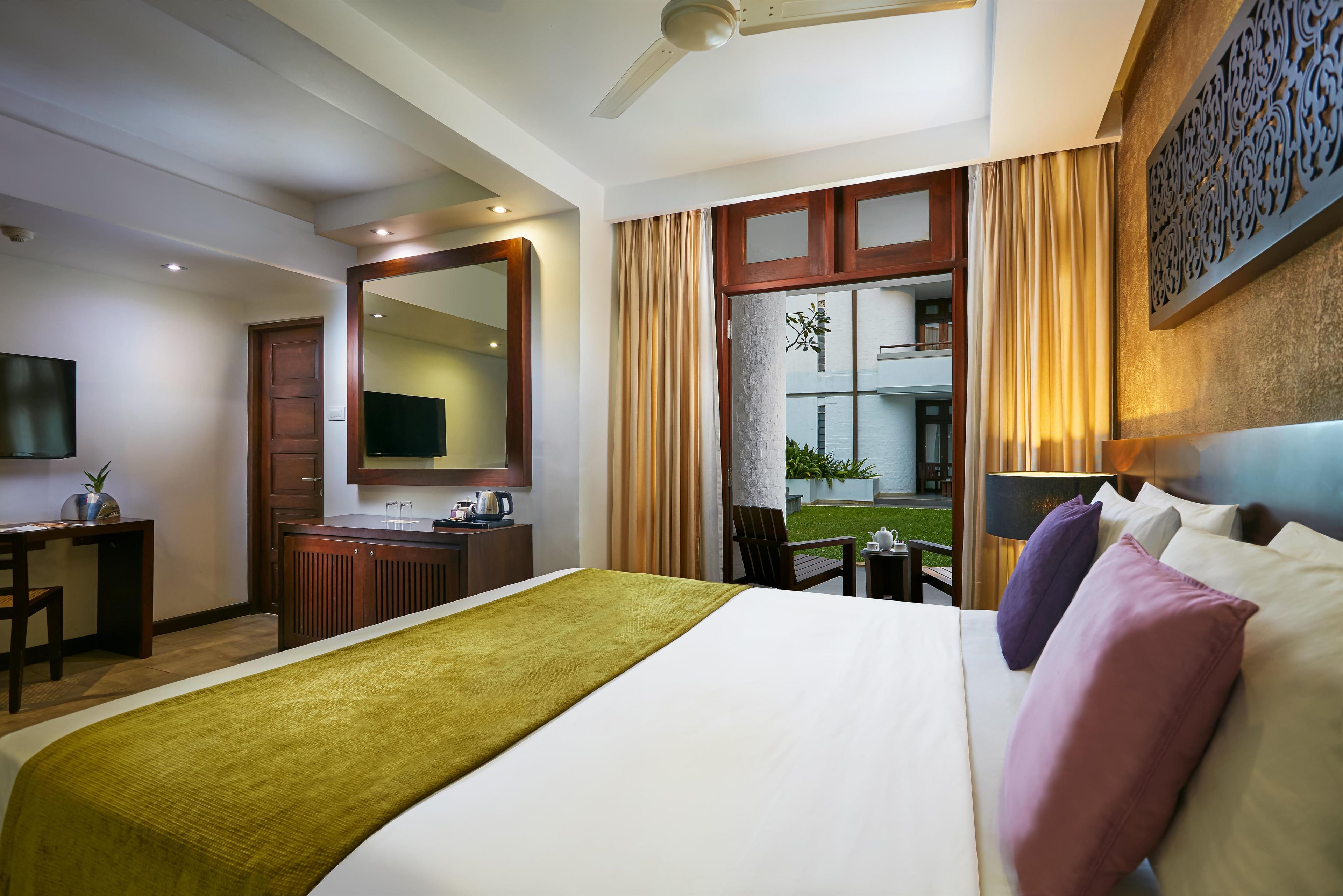 A hotel room with a bed, a desk, a television, a mirror, and a view of the outside.