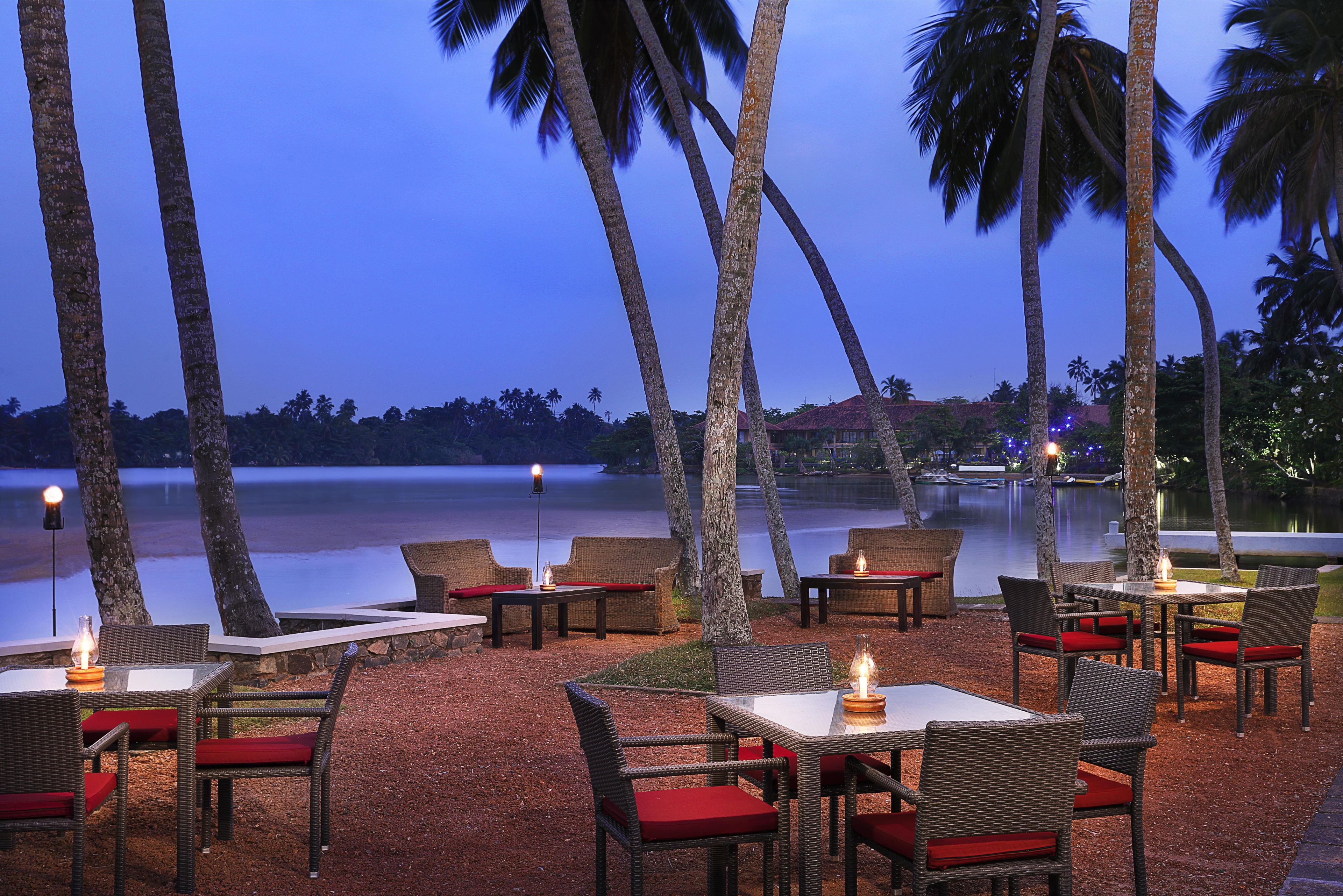 An outdoor seating area with wicker furniture and red cushions, overlooking a body of water.