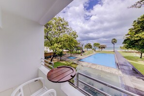 Relax on the balcony with a view of the pool surrounded by lush greenery and trees.