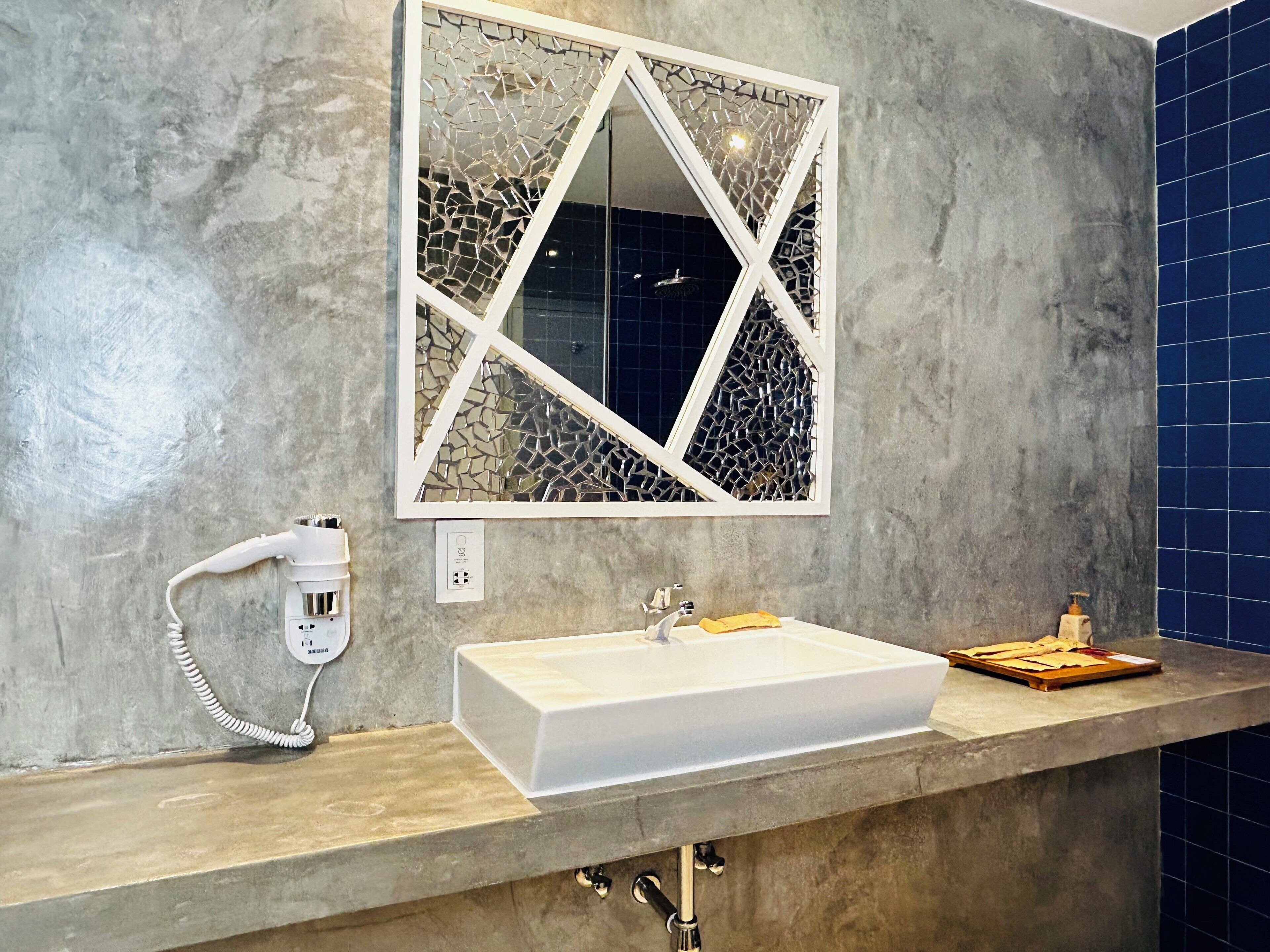 A bathroom with a white sink, a mirror with a geometric pattern, and a blue tiled wall.