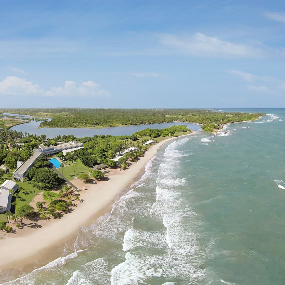 An aerial view of a coastal property with a beach, a large building, and a lake.