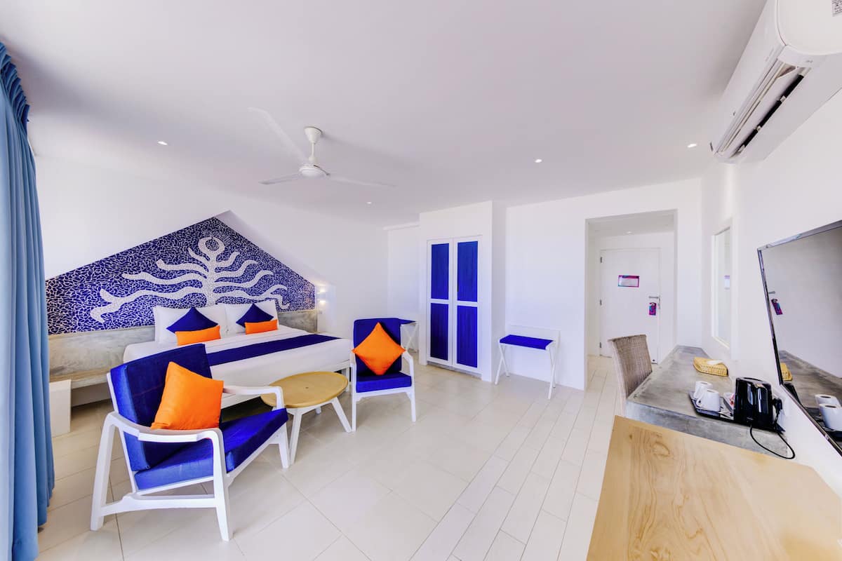 A modern hotel room with a bed, a sofa, two armchairs, a small table, and a TV.