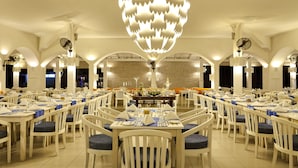 A spacious dining area with multiple tables and chairs, a central chandelier, and a clock on the wall. - Trinco Blu by Cinnamon (Trincomalee)
