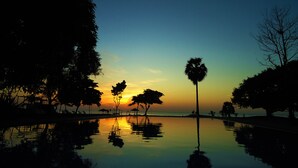 A serene sunset over a calm pool with trees and lounge chairs. - Trinco Blu by Cinnamon (Trincomalee)