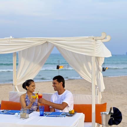 A beachside dining setup with a table, white drapes, and a view of the ocean.