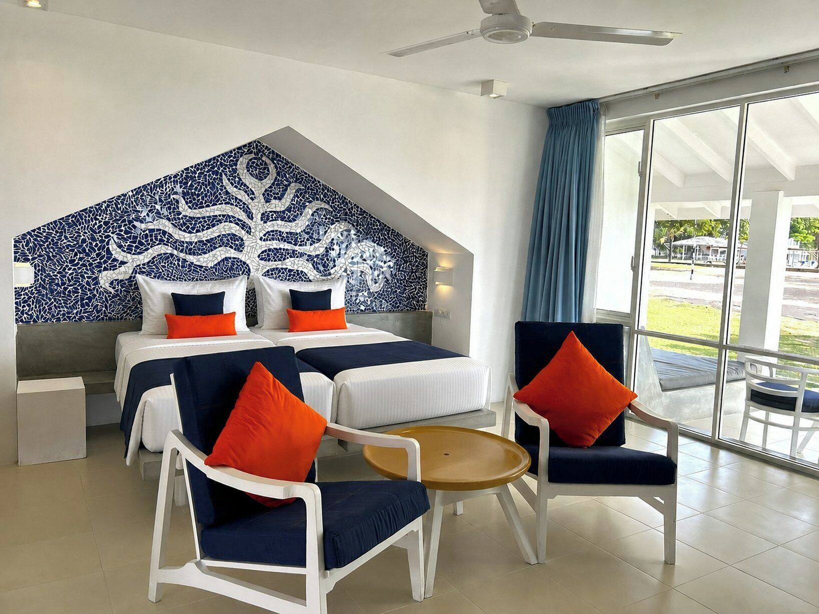 A hotel room with a bed, two chairs, a small table, and a large window with curtains.