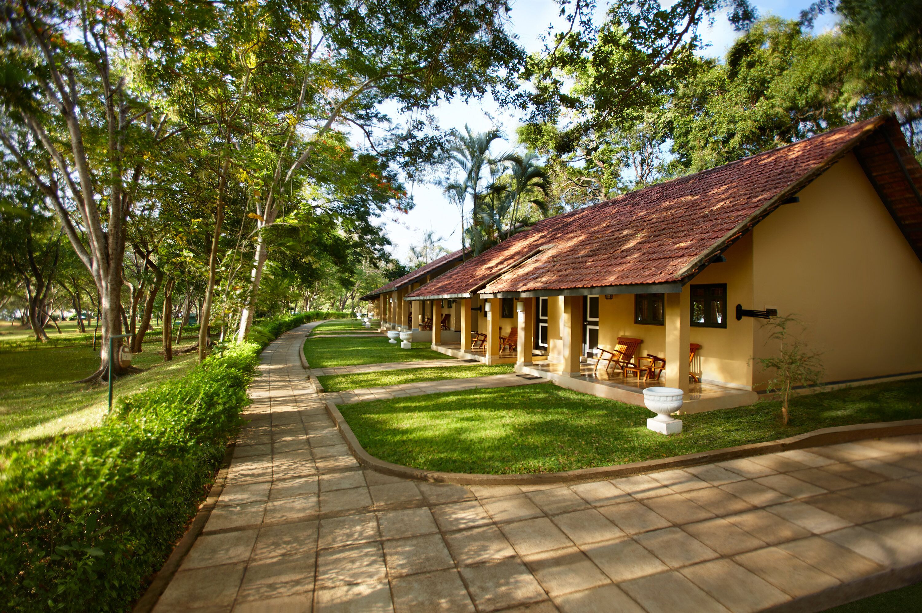 A row of yellow buildings with red roofs, surrounded by lush greenery and a paved walkway.