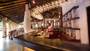 A bar area with a bartender preparing drinks, wooden shelves with bottles, and hanging glassware. - Habarana Village by Cinnamon (Habarana)