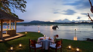 A dining table set for two with a view of a lake and a distant elephant. - Habarana Village by Cinnamon (Habarana)