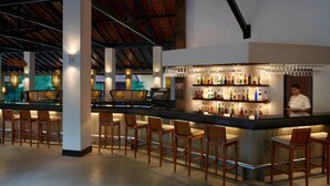 A bar area with wooden bar stools, a counter with bottles, and a person behind the bar. - Habarana Village by Cinnamon (Habarana)