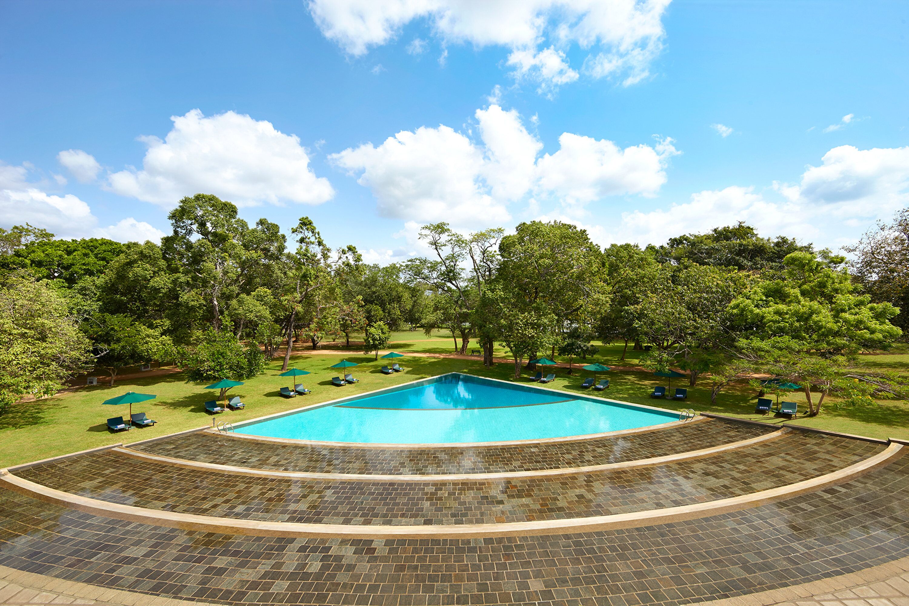 A swimming pool with a tiled deck, surrounded by green grass and trees.