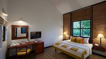 Une chambre d’hôtel équipée d’un lit, d’un bureau, d’une chaise, d’une télévision et d’une fenêtre donnant sur un paysage arboré.