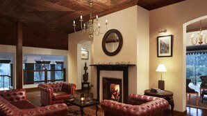 A cozy living room with leather armchairs, a fireplace, and a chandelier. - Jetwing St. Andrew's (Nuwara Eliya)