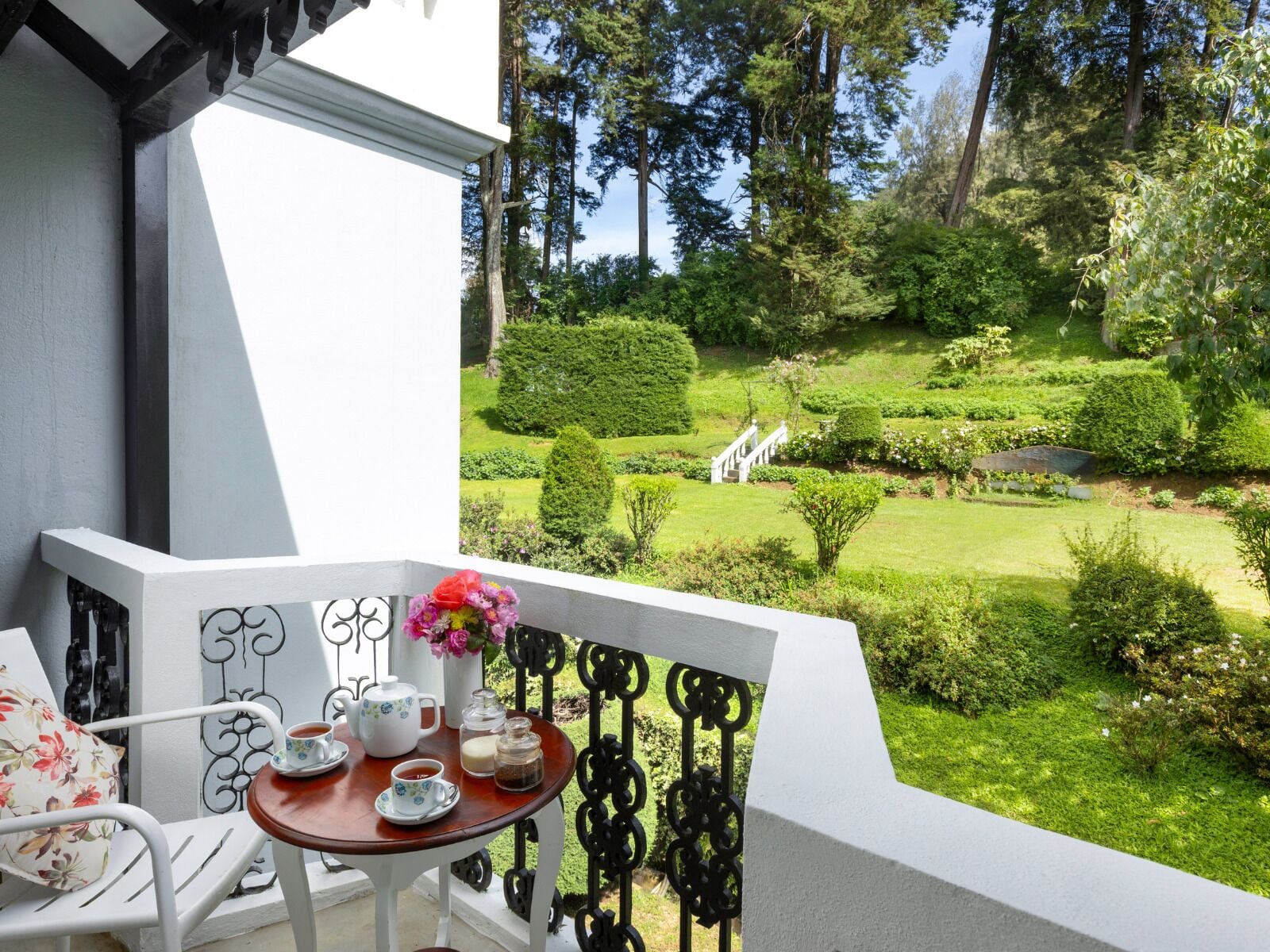 Ein Balkon mit Tisch, der für Tee gedeckt ist, einem Stuhl und Blick auf einen gepflegten Garten.