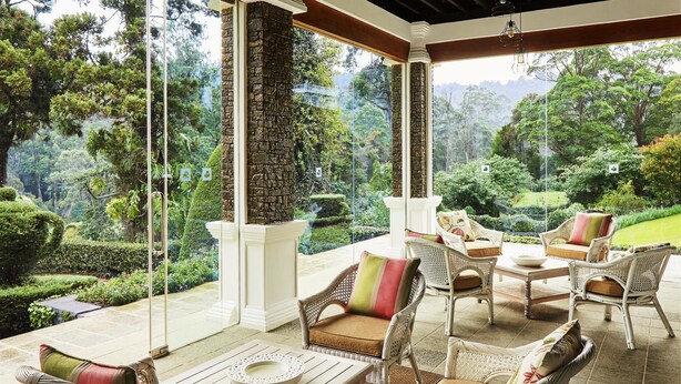 A covered patio with wicker furniture, stone pillars, and a view of lush greenery. - Jetwing St. Andrew's (Nuwara Eliya)