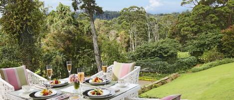 Mesa de comedor al aire libre con sillas de mimbre blancas, platos de fruta y copas de champán.