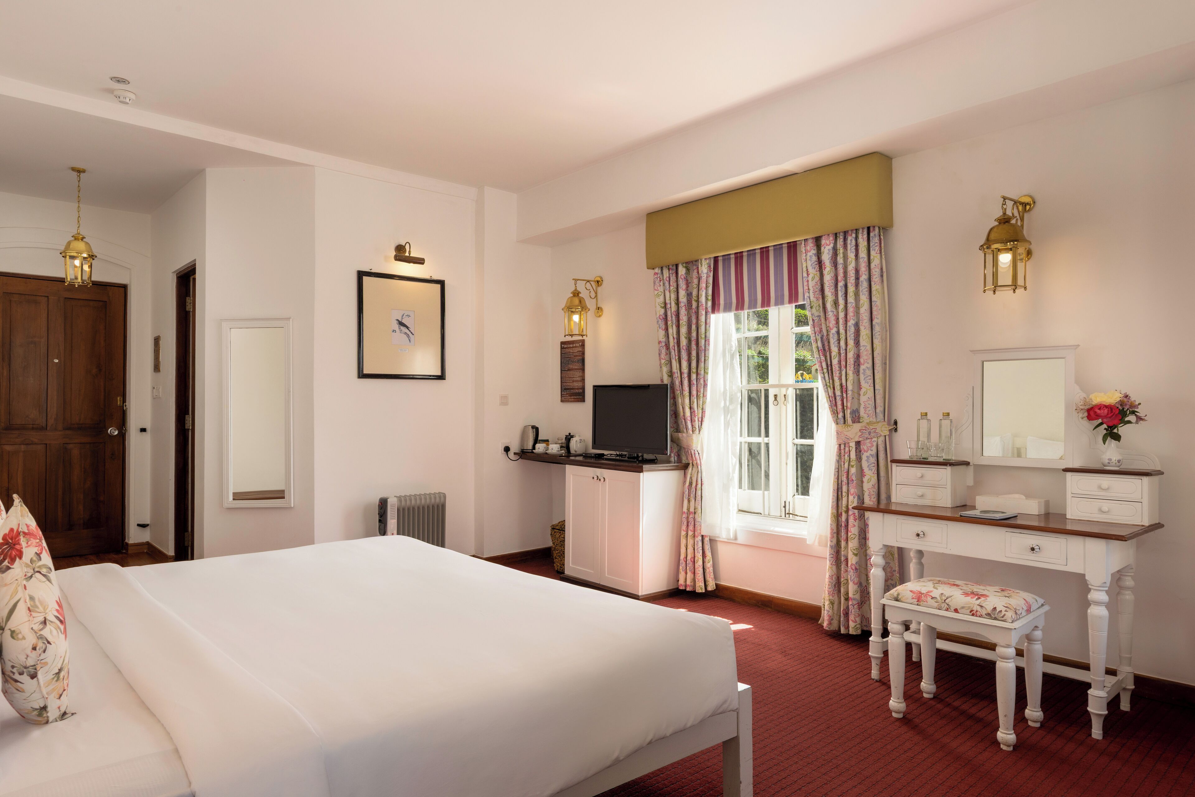 A hotel room with a bed, a desk with a mirror, a television, and a window with curtains.