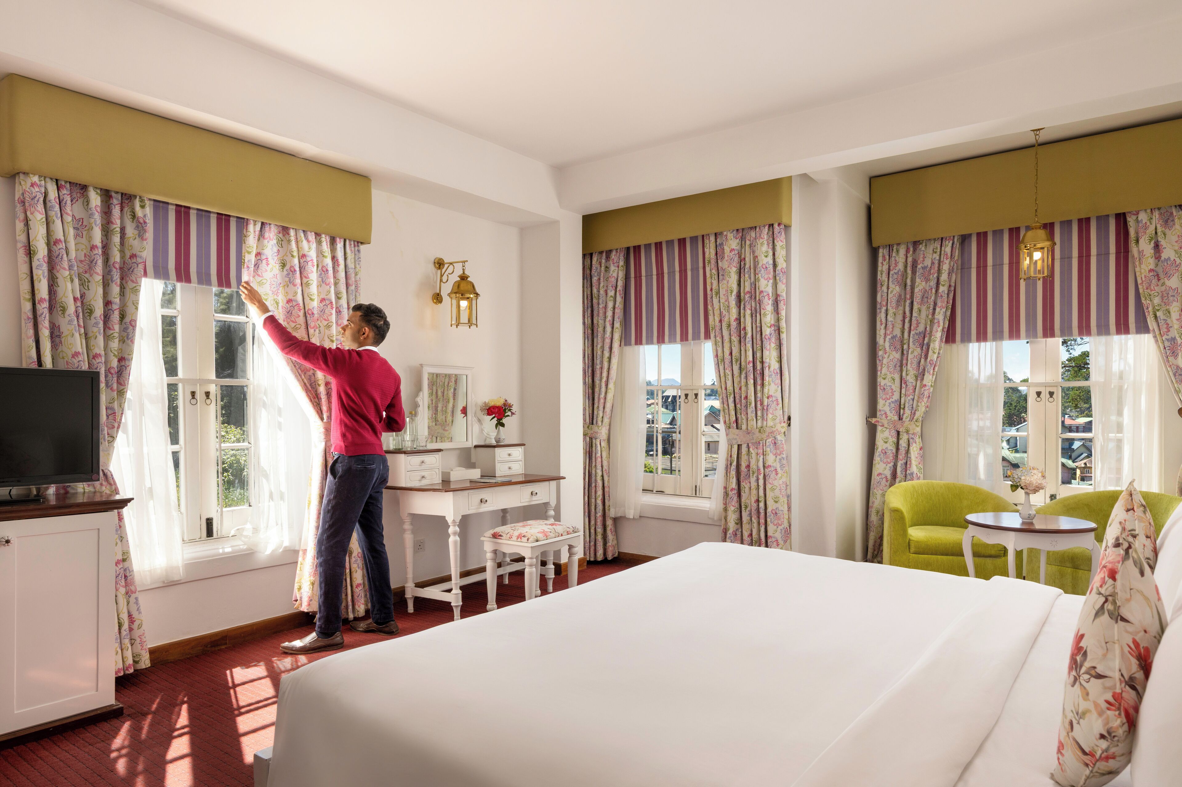 A hotel room with a bed, a desk, a chair, a television, and curtains.