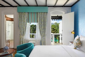 A bedroom with a bed, a window with curtains, a view of greenery, a bathroom with a shower, and a balcony with a railing. - Jetwing St. Andrew's (Nuwara Eliya)