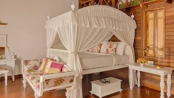 Un lit à baldaquin à quatre poteaux recouvert d’un tissu à motifs floraux, une table de chevet blanche et un plancher en bois.