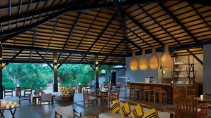 An outdoor seating area with wooden furniture, a bar, and hanging light fixtures. - Cinnamon Wild Yala (Kirinda)