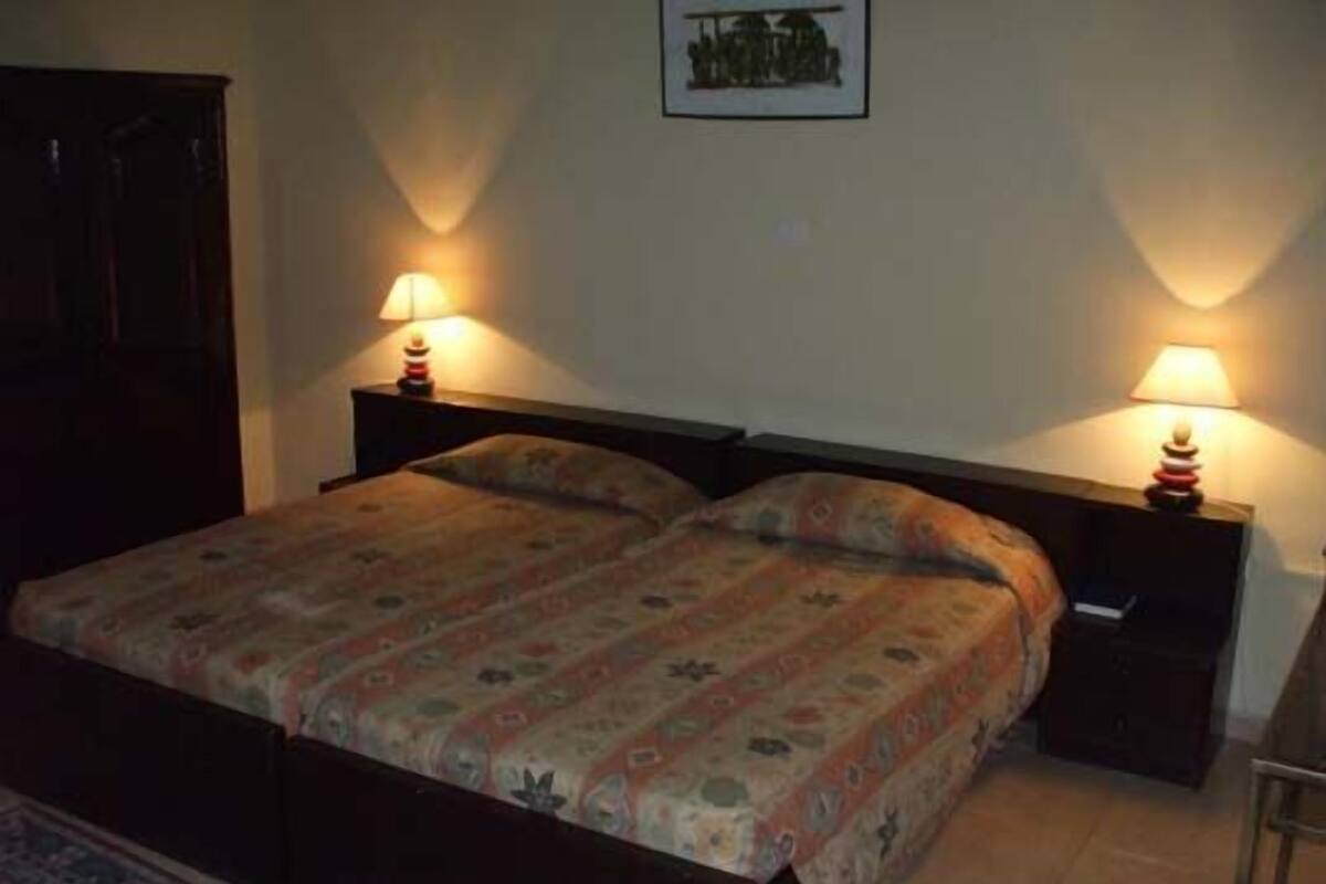 A bedroom with a bed, two bedside tables with lamps, a nightstand, a door, and a framed picture on the wall.