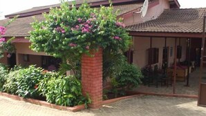 A house with a brick pillar, a satellite dish, and a garden with various plants and flowers. - Coconut Grove Miners Lodge (Obuasi)