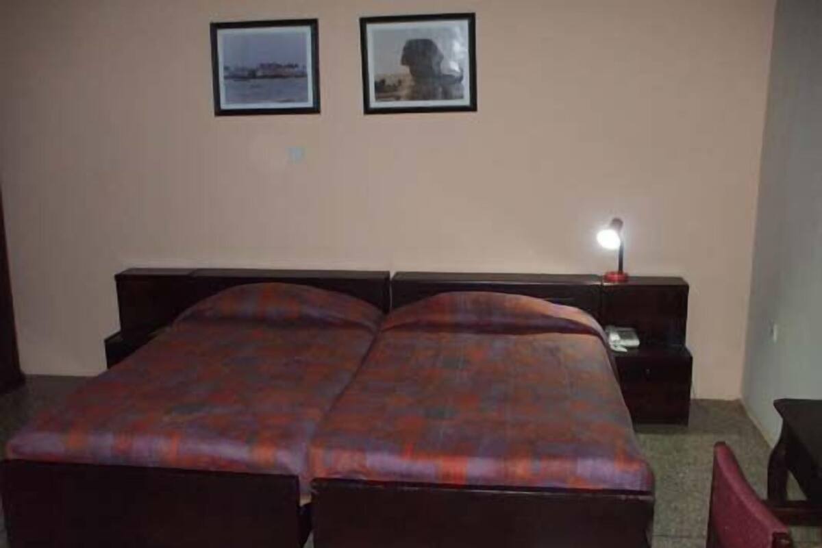 A double bed with a plaid bedspread, a bedside table with a lamp, and two framed pictures on the wall.