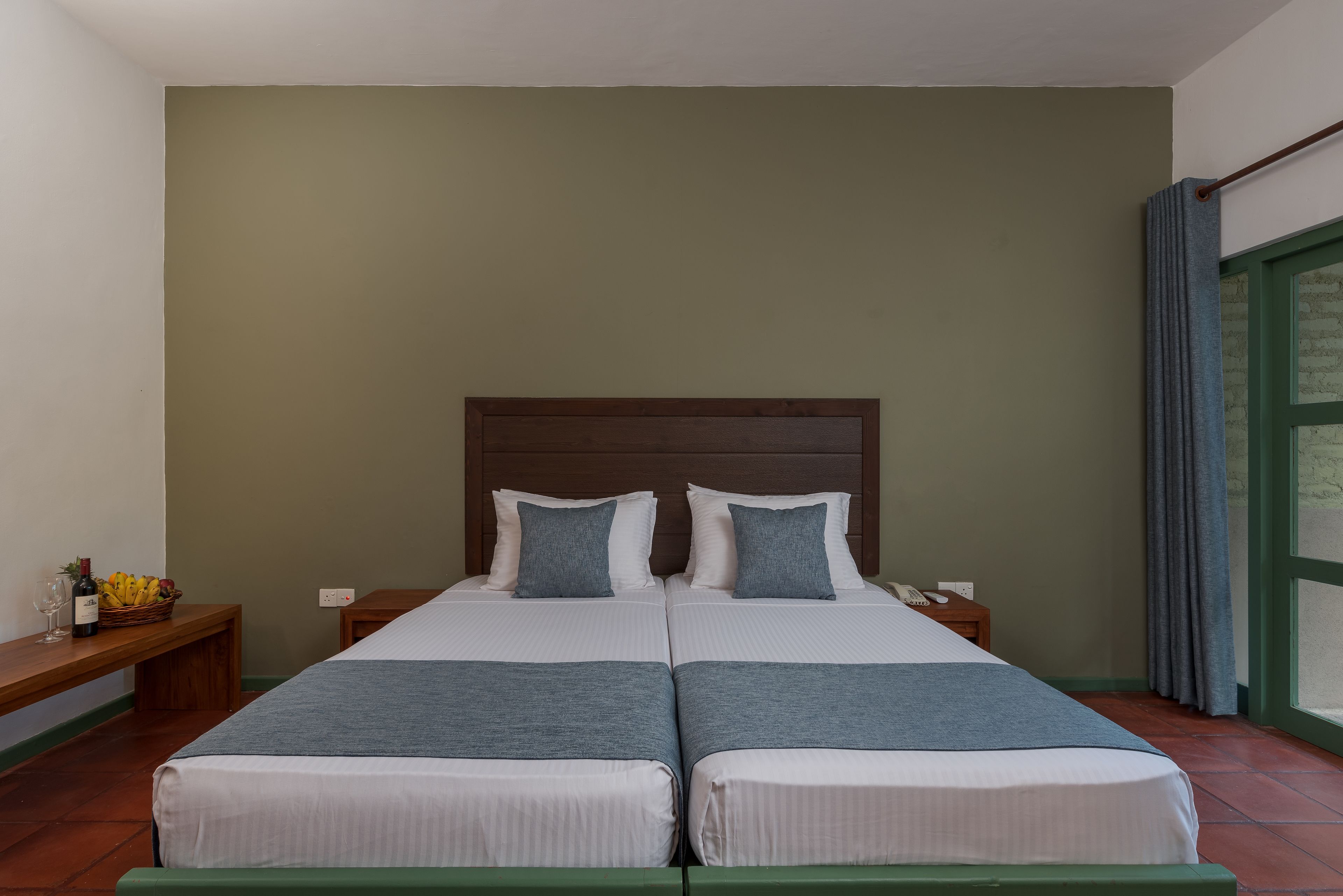 A double bed with a wooden headboard, two pillows, and a bedside table with a phone and a basket of fruit.