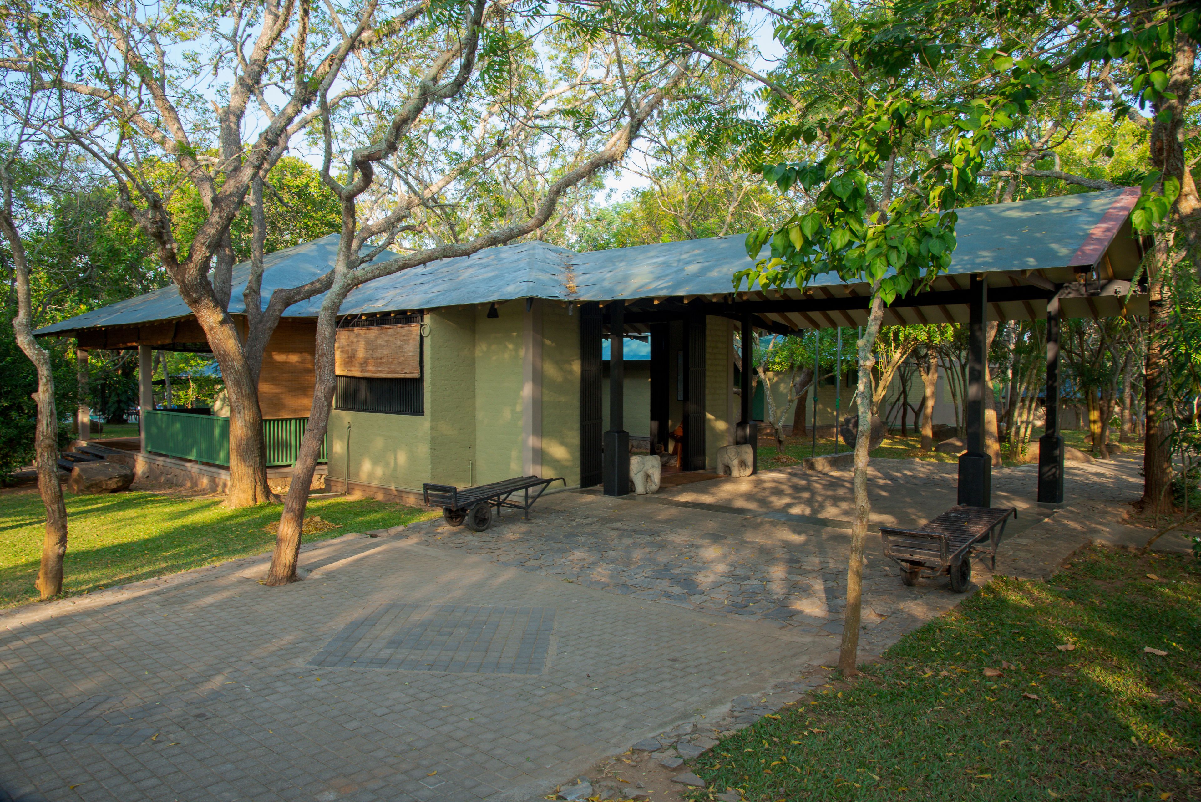 A covered outdoor area with benches and a picnic table, surrounded by trees.