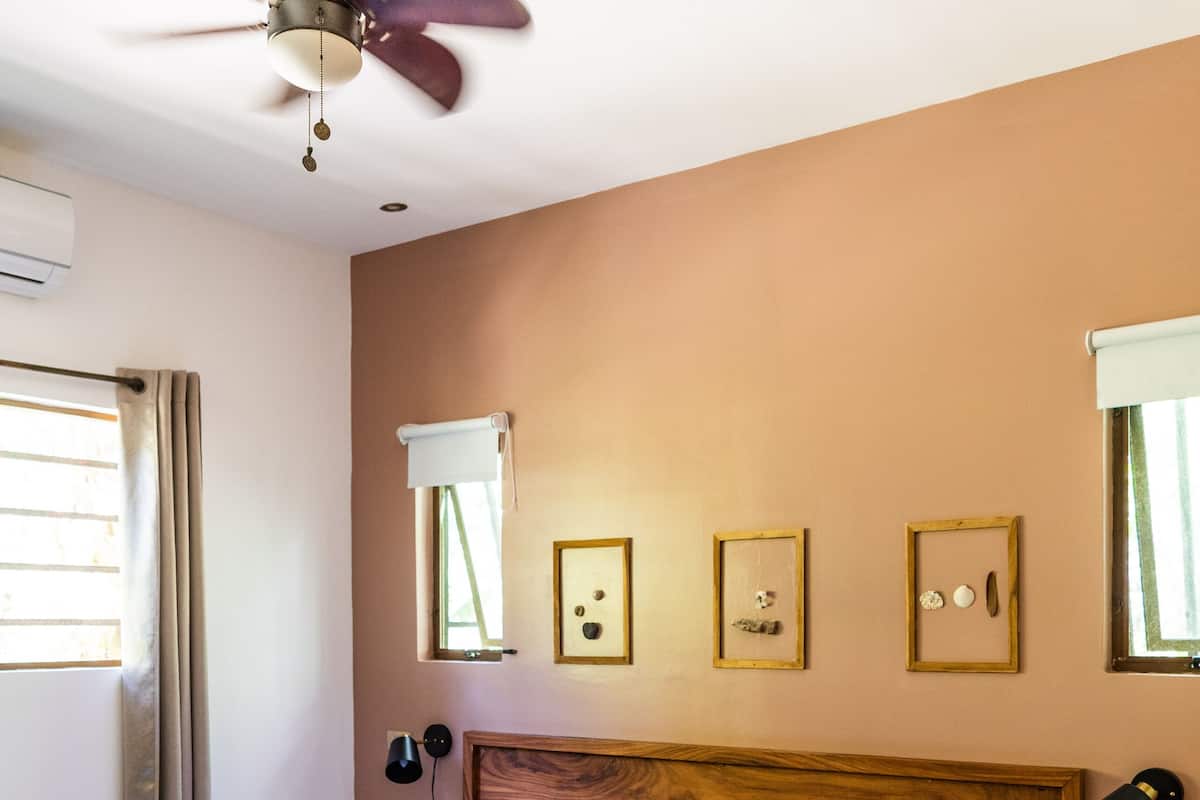 A neatly made bed with white linens and a brown headboard, a ceiling fan, and framed pictures on the wall.
