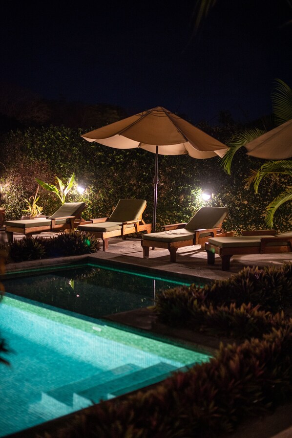A nighttime pool area with lounge chairs and umbrellas.