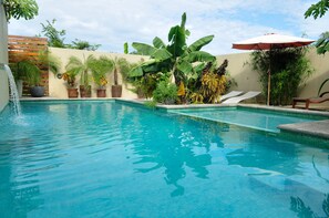 A swimming pool with a water fountain, surrounded by potted plants and a wooden fence.