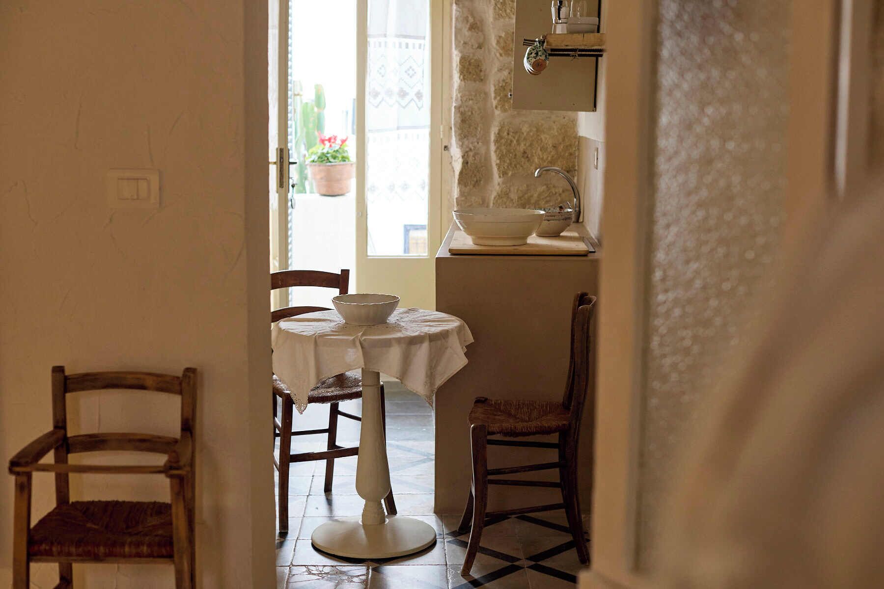 A narrow hallway with a table and chairs, a potted plant, and a window with a view of a building.