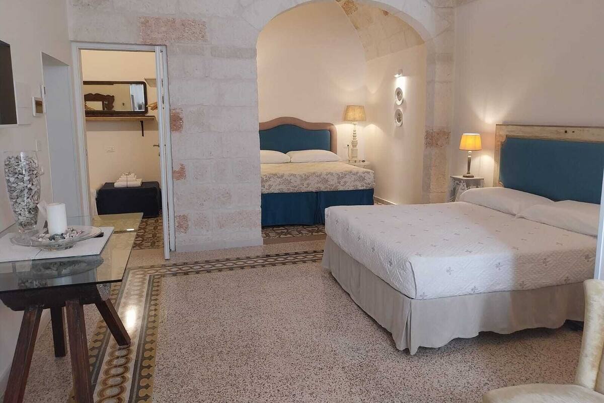 Une chambre d’hôtel avec deux lits, une petite table sur laquelle se trouve un vase, et un miroir.