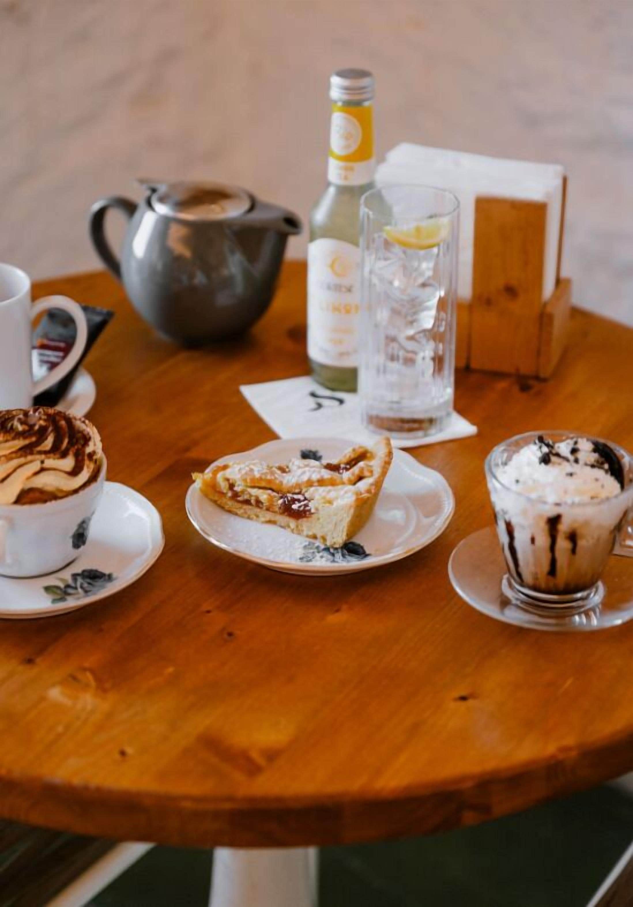 A wooden table with a teapot, a bottle, a glass of water, and two plates with desserts.