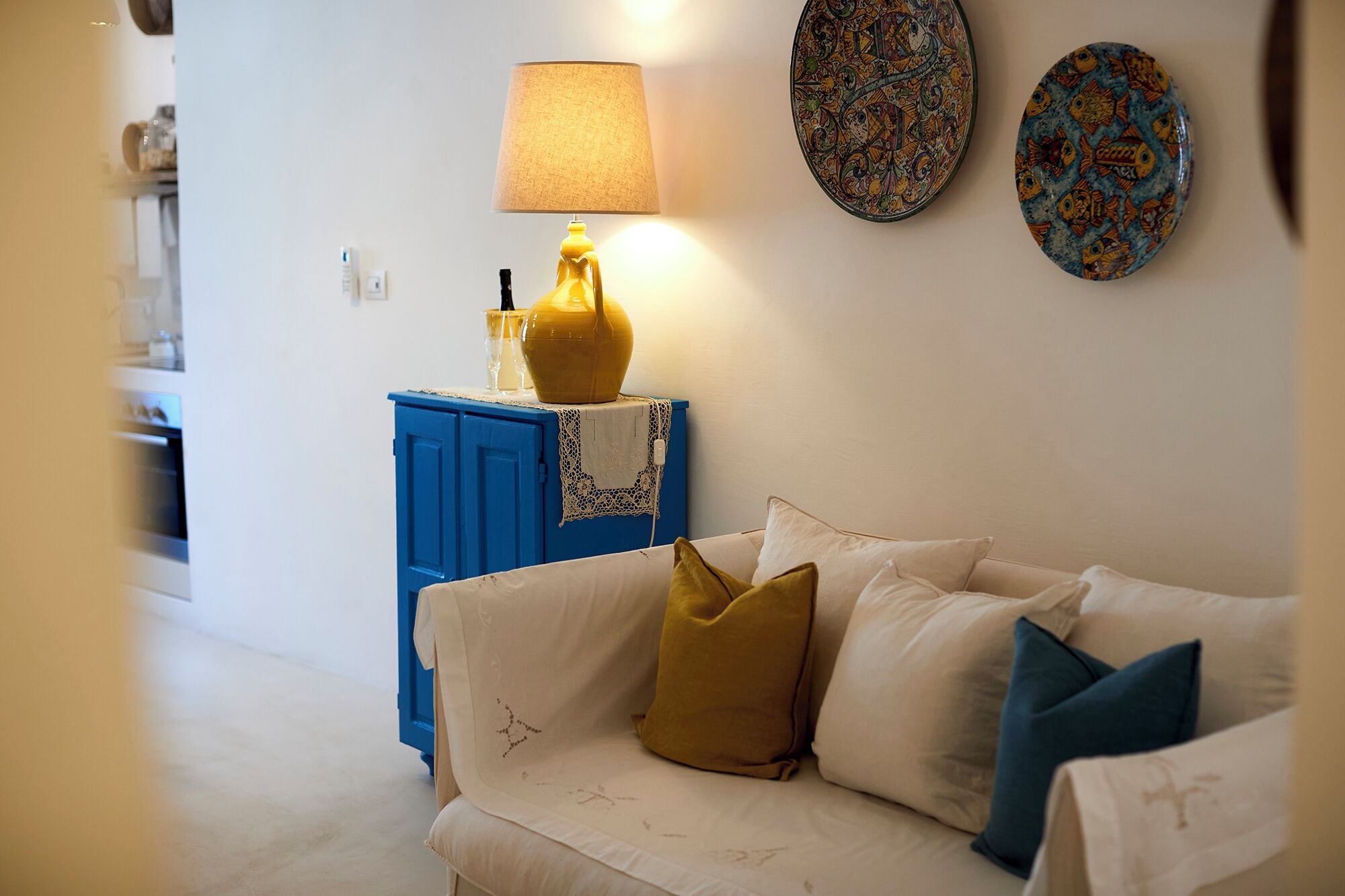 A living room with a white sofa, a blue cabinet, a yellow lamp, and two decorative plates on the wall.
