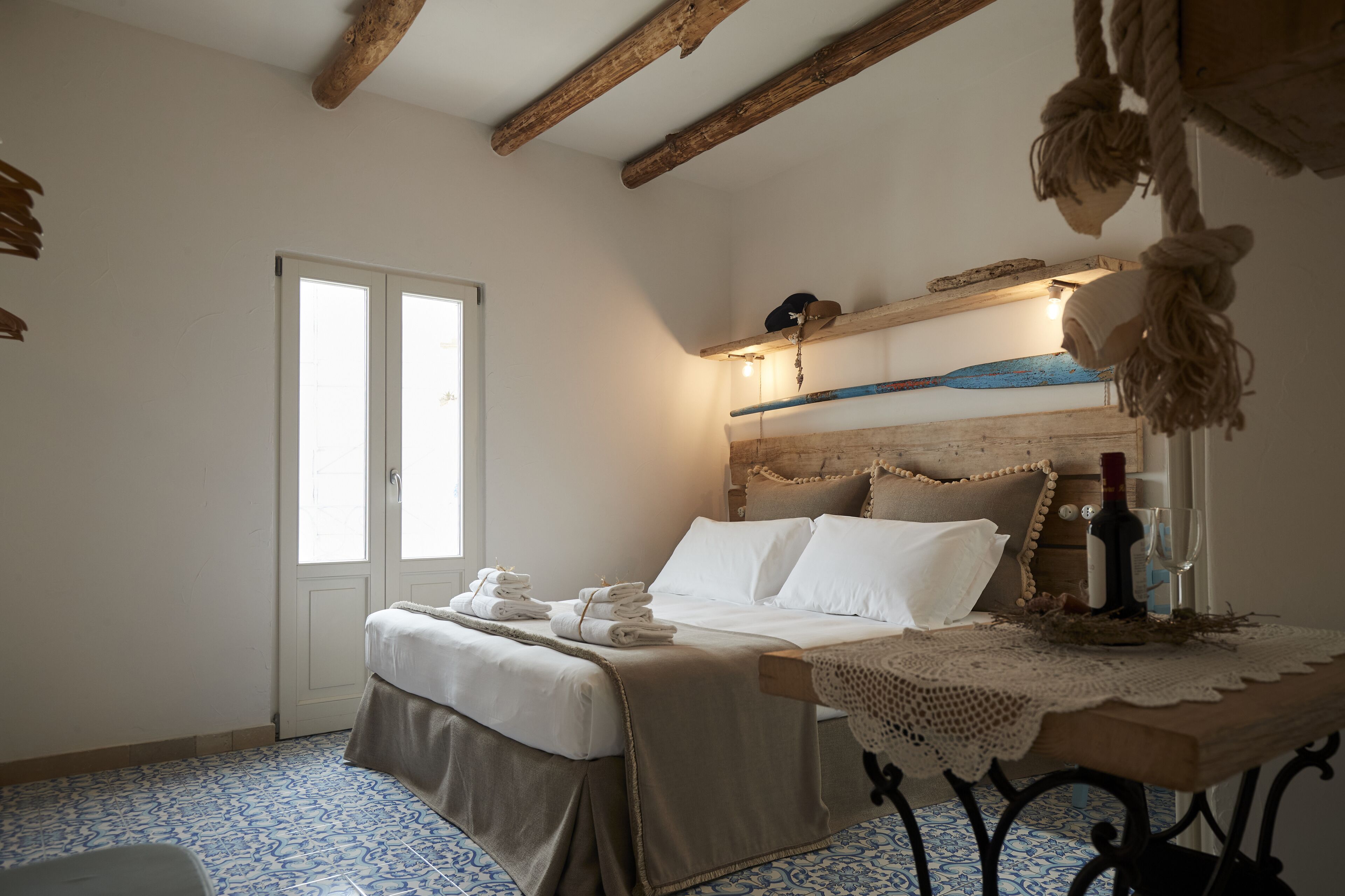 A bedroom with a bed, a bedside table with a bottle and glass, a window, and a door.