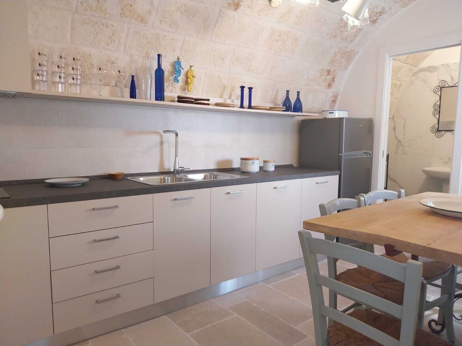A modern kitchen with white cabinets, a stainless steel sink, and a wooden dining table.
