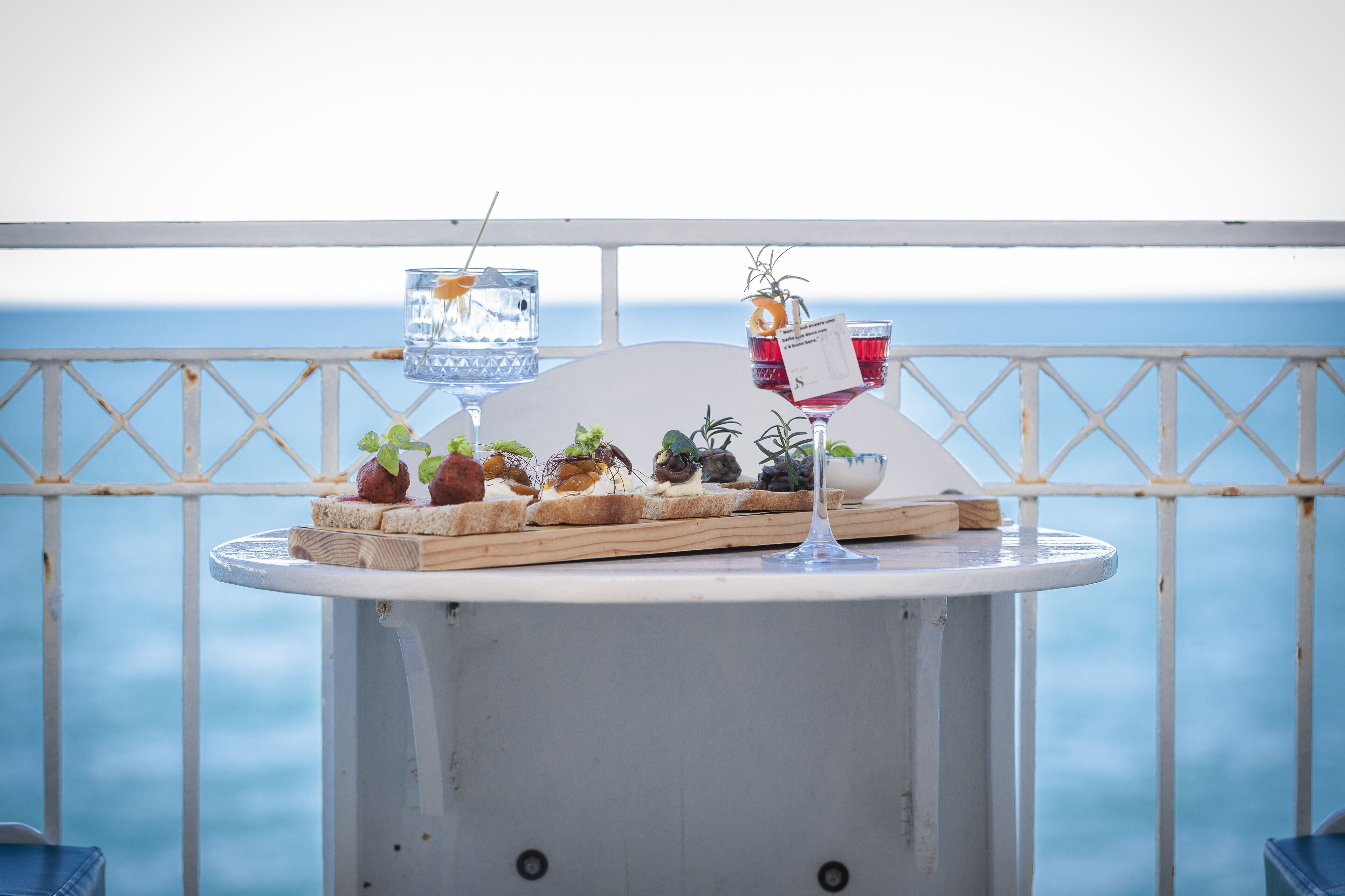 A table with food and drinks on a balcony with a view of the sea.