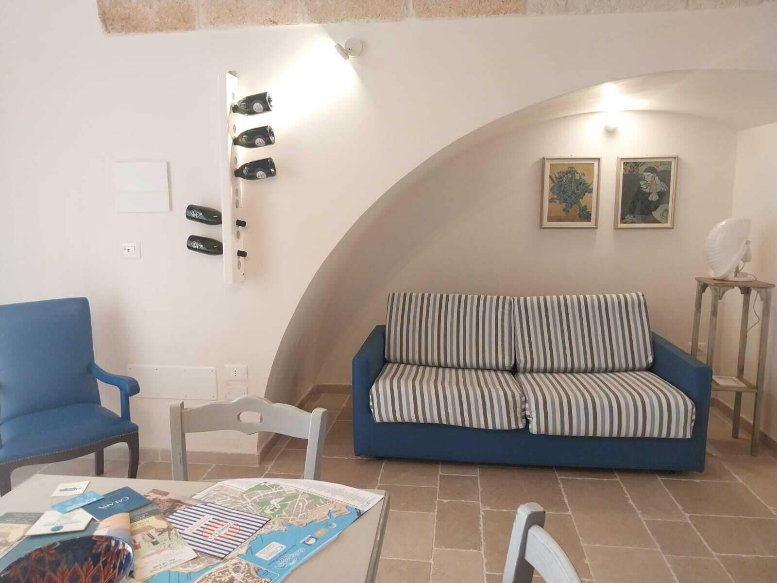 Ein Wohnzimmer mit blauem Sofa, blauem Sessel, einem Esstisch mit einer Karte und einem an der Wand montierten Weinkühler.