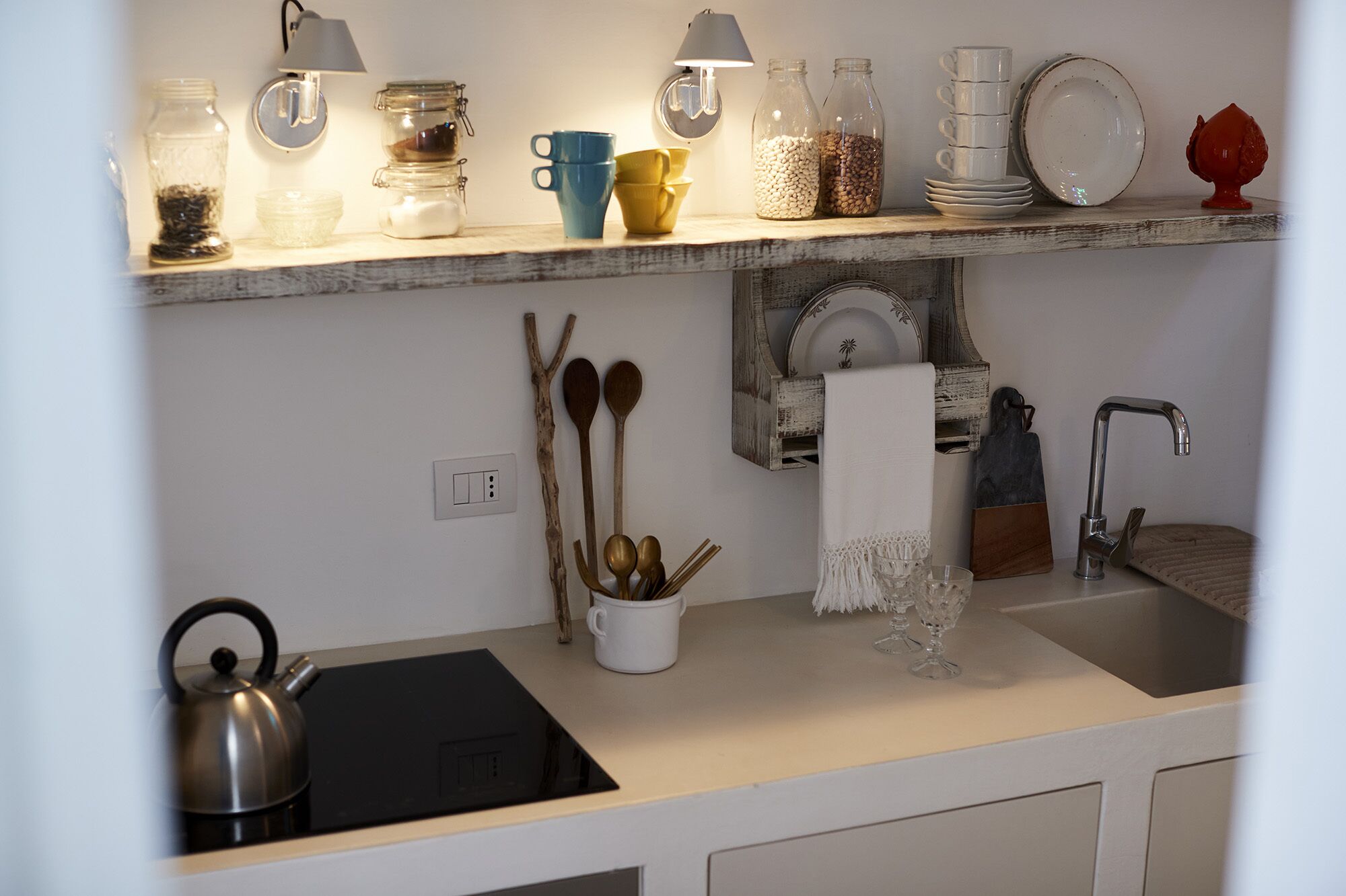 A kitchen with a black induction cooktop, a sink, and a wooden spoon hanging on the wall.