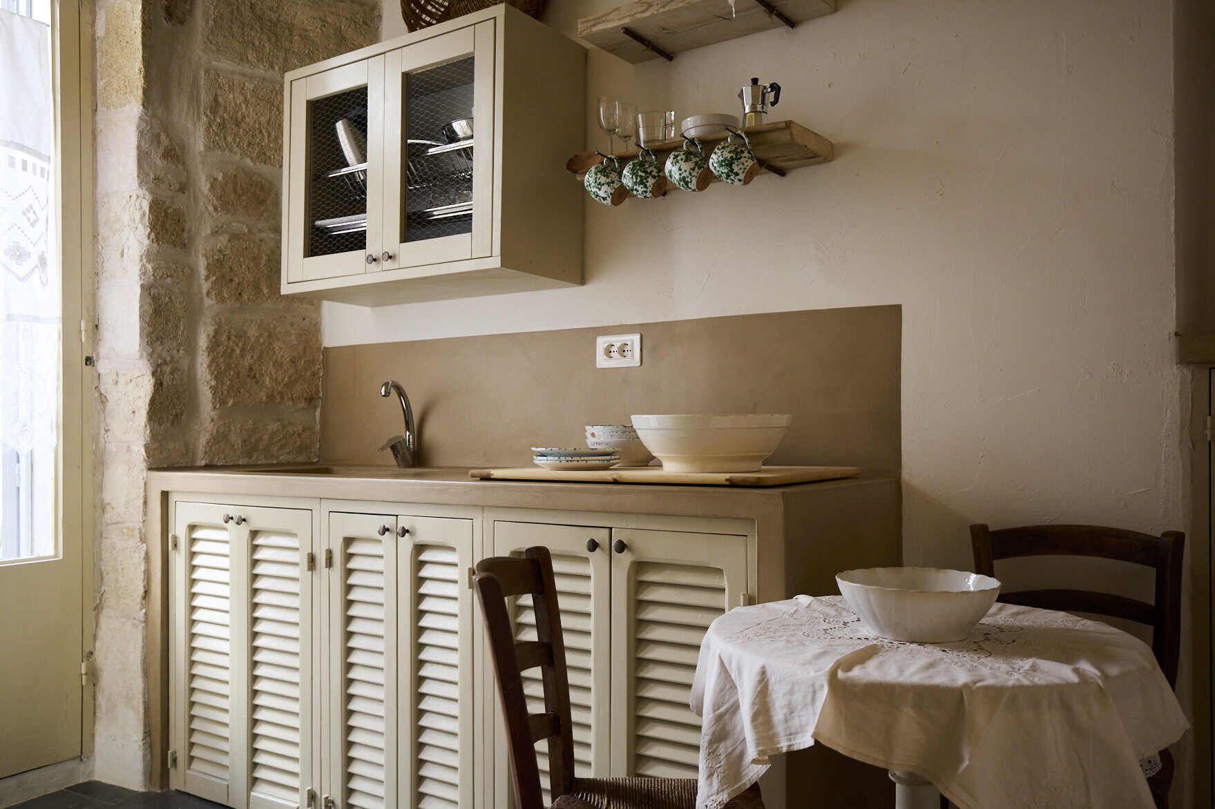 A kitchen with a stone wall, a wooden cabinet with glass doors, a sink, and a table with a white tablecloth.