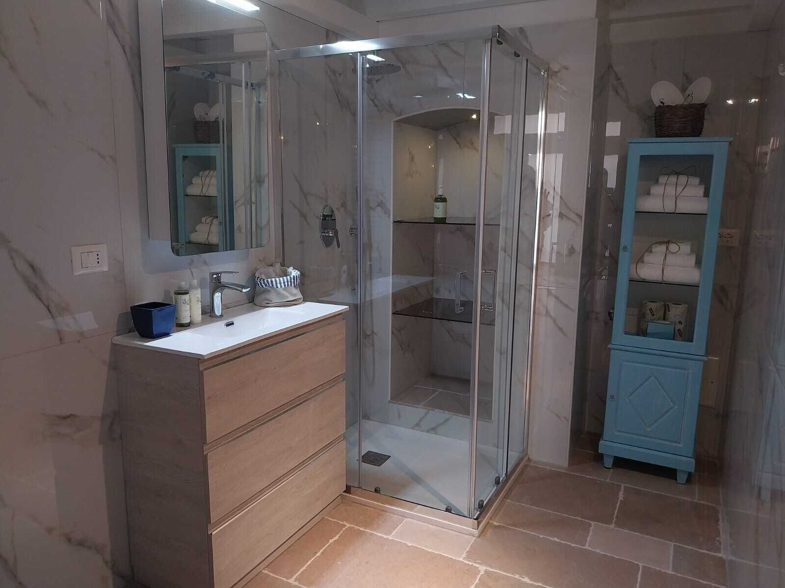 Une salle de bain moderne avec une douche à parois de verre, un meuble-lavabo en bois et un meuble bleu contenant des serviettes.