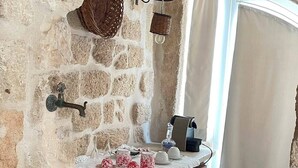 Un baño de paredes de piedra con lavamanos, lámpara colgante y ventana con cortinas.