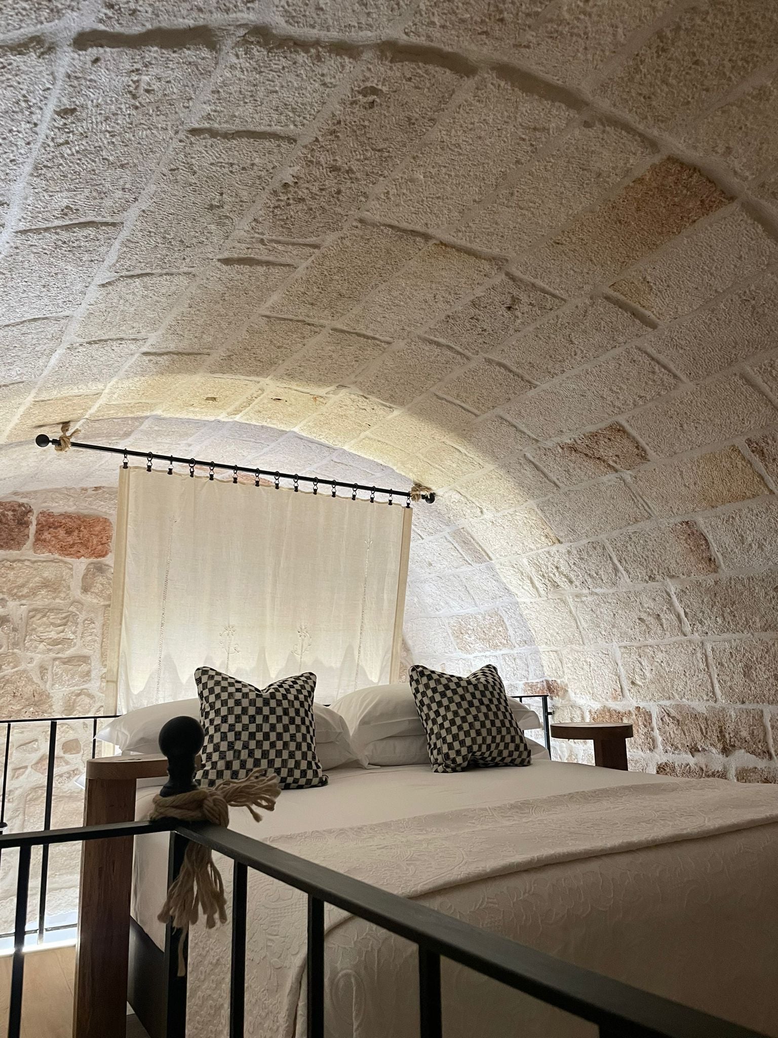 A bedroom with a stone ceiling, a bed with checkered pillows, a canopy, and a nightstand.