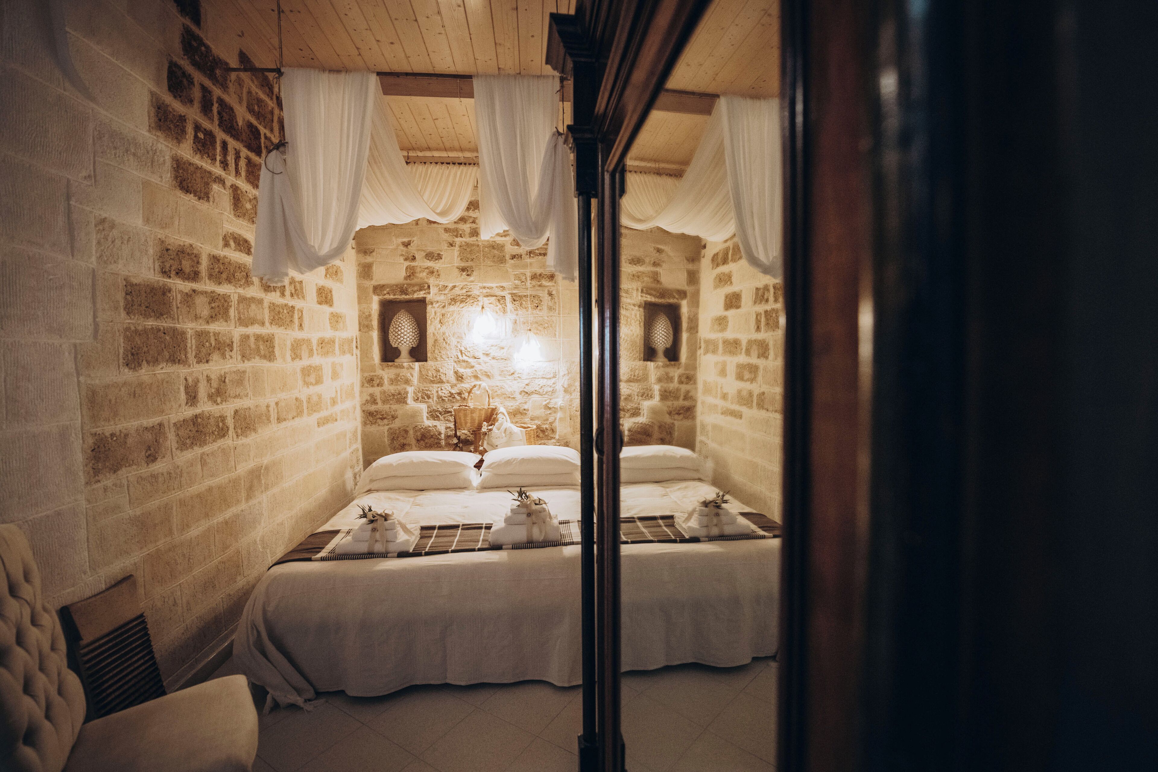 Una habitación con paredes de piedra, dos camas, cortinas blancas y techo de madera.