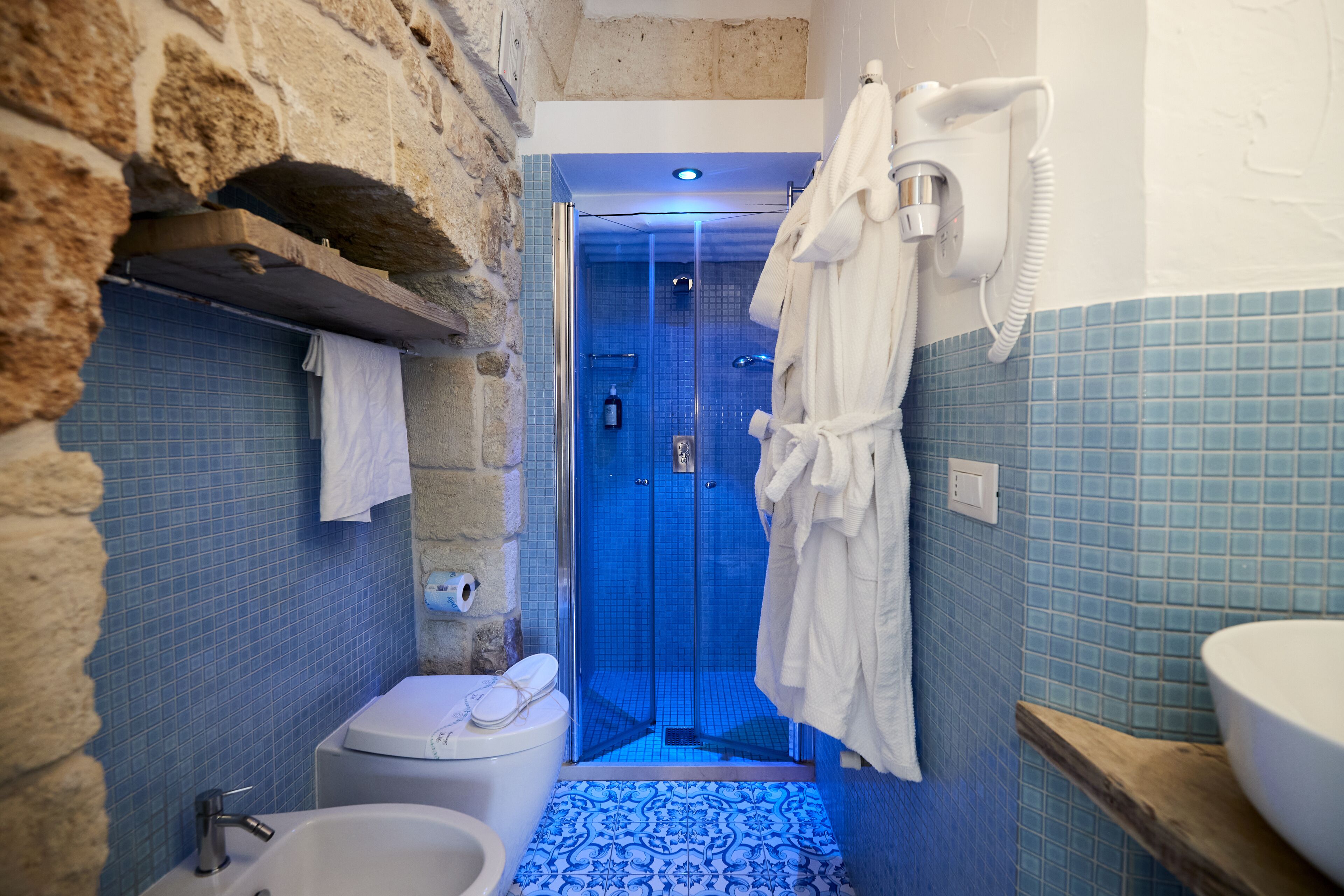 Un baño con piso de azulejos azules, una bañera blanca, un inodoro y una zona de ducha con mampara de vidrio.