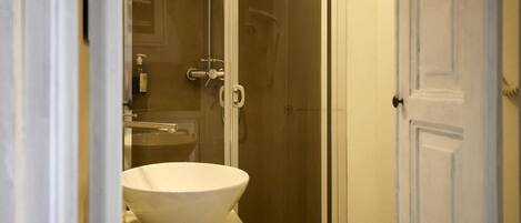Une salle de bain avec un lavabo blanc, une cabine de douche en verre et une porte blanche.
