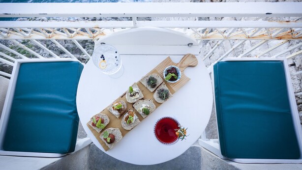 Una mesa con varios aperitivos y una bebida, situada en un balcón con vista al océano.